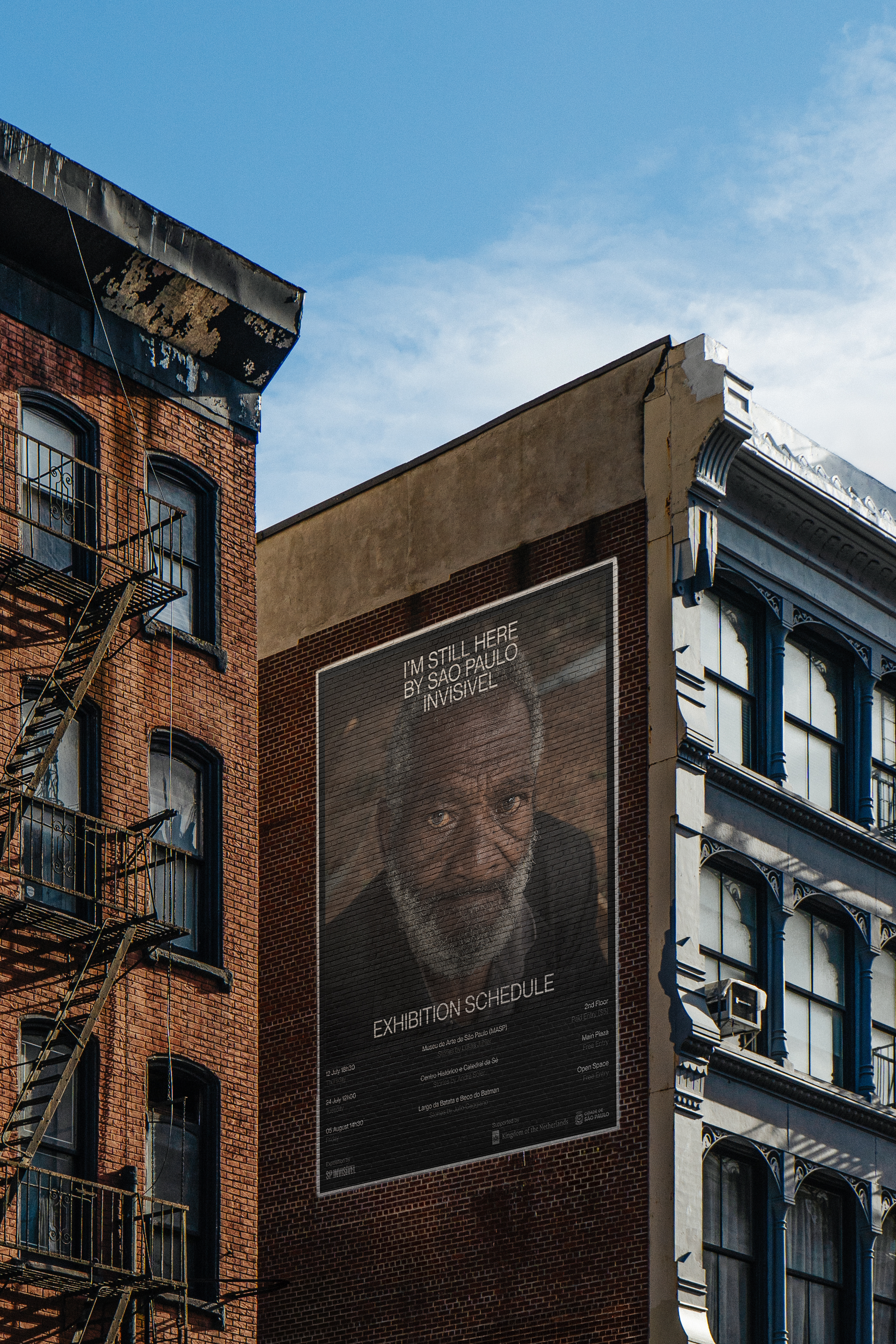 SP Invisível exhibition poster on a New York building, featuring a portrait and the title I'm Still Here.
